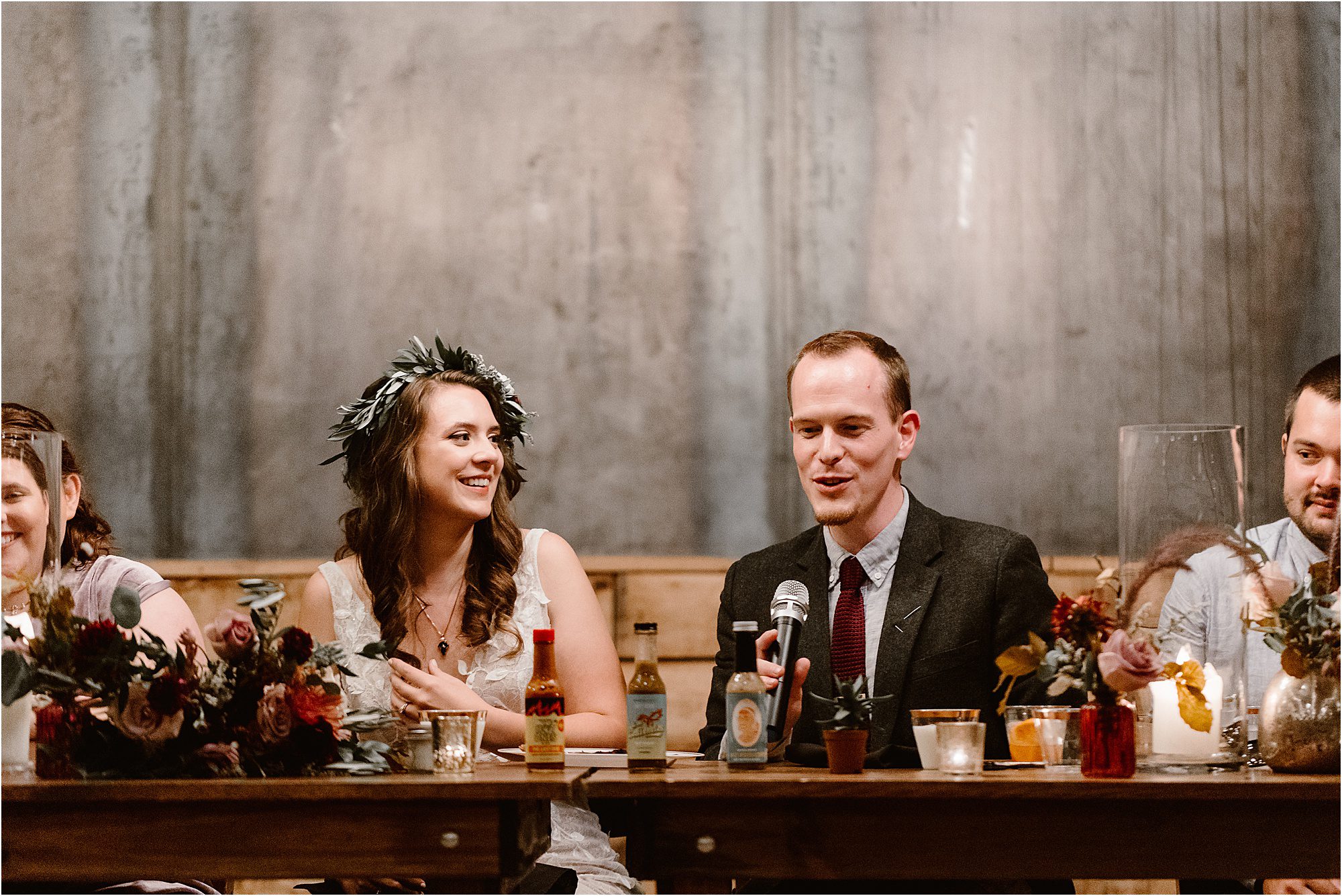 groom talks into microphone at wedding reception while seated at table