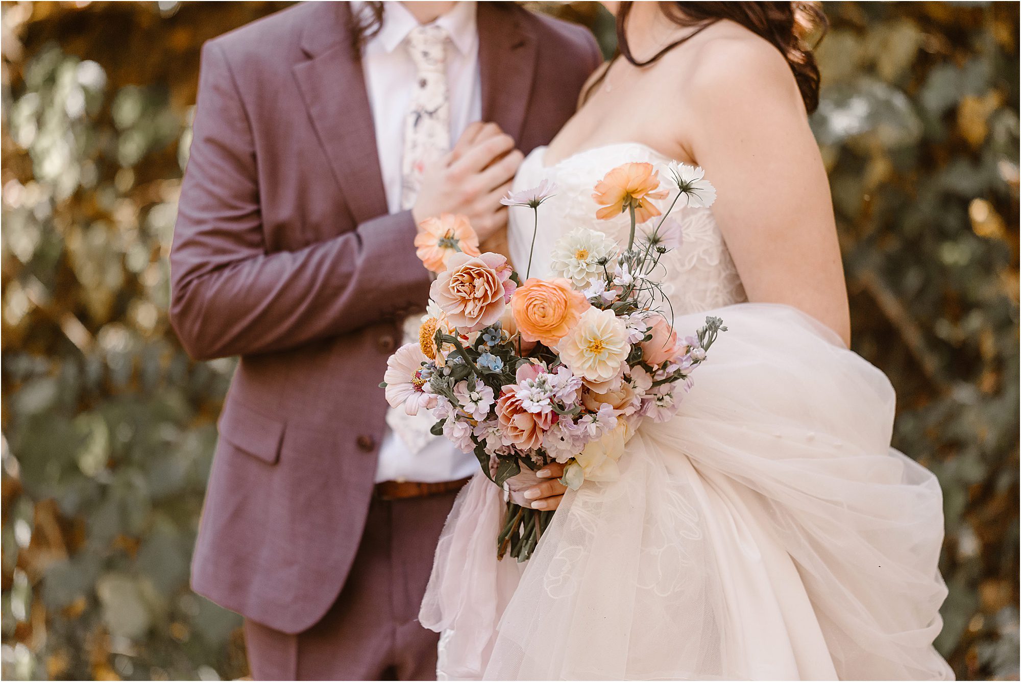 bride and groom hold fall wedding bouquet against strapless wedding dress and burgundy suit with floral tie