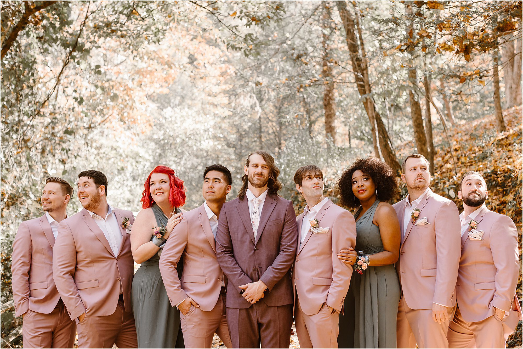 groom standing with wedding party in pink and burgundy suits and green dresses