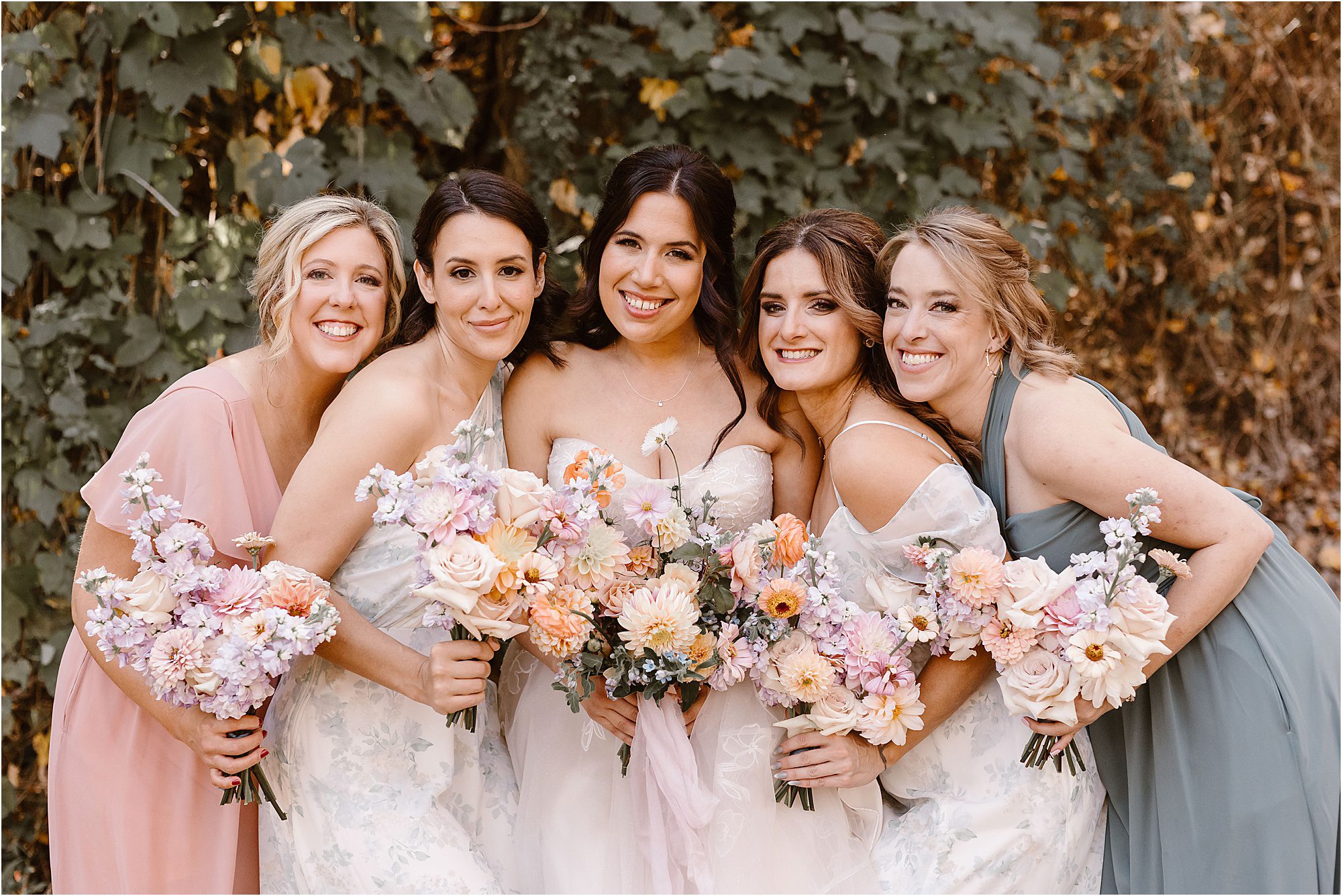 bride smiles with bridesmaids in floral bridesmaid dresses holding large fall wedding bouquets
