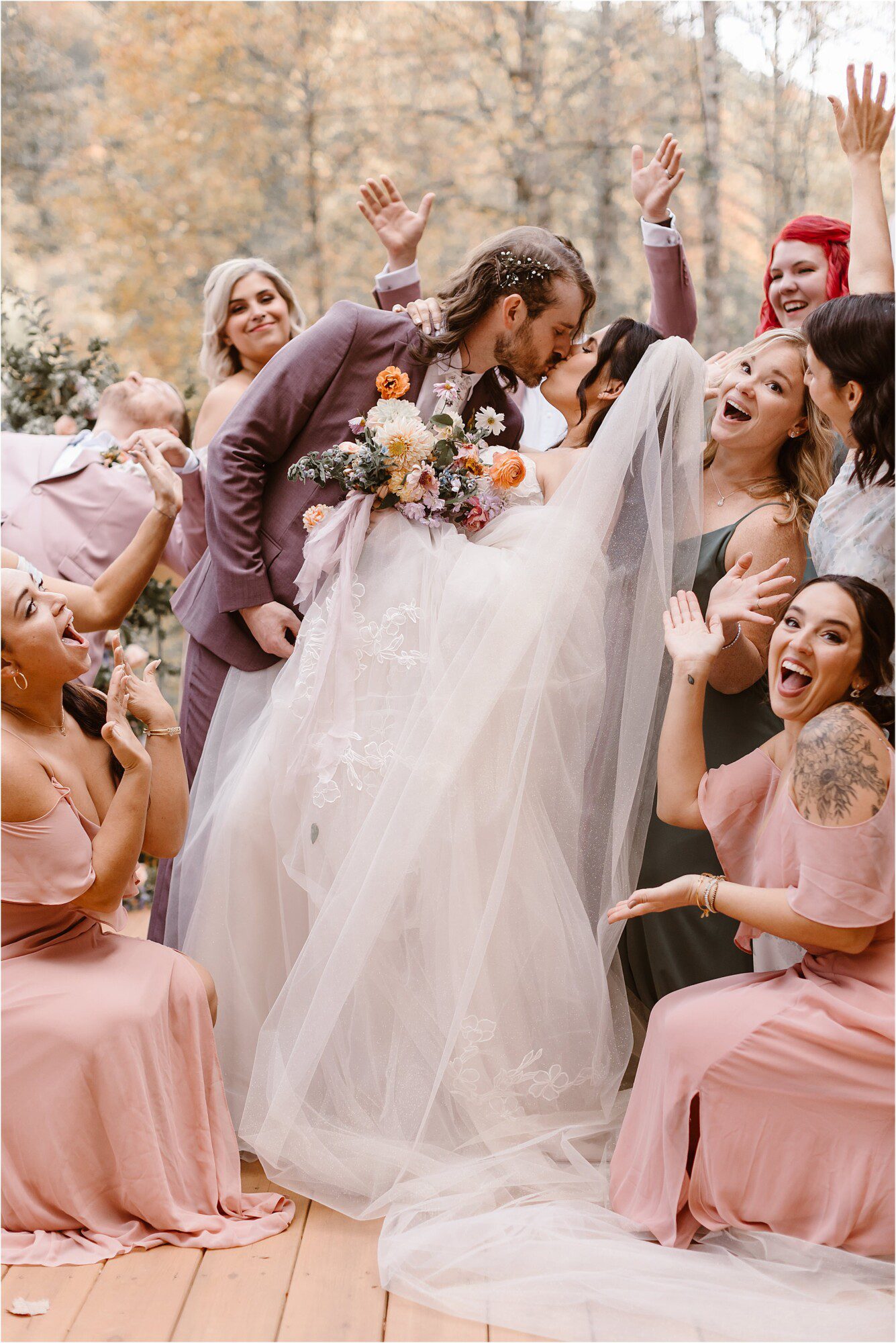 groom dips back bride and kisses her surrounded by bridesmaids and groomsmen