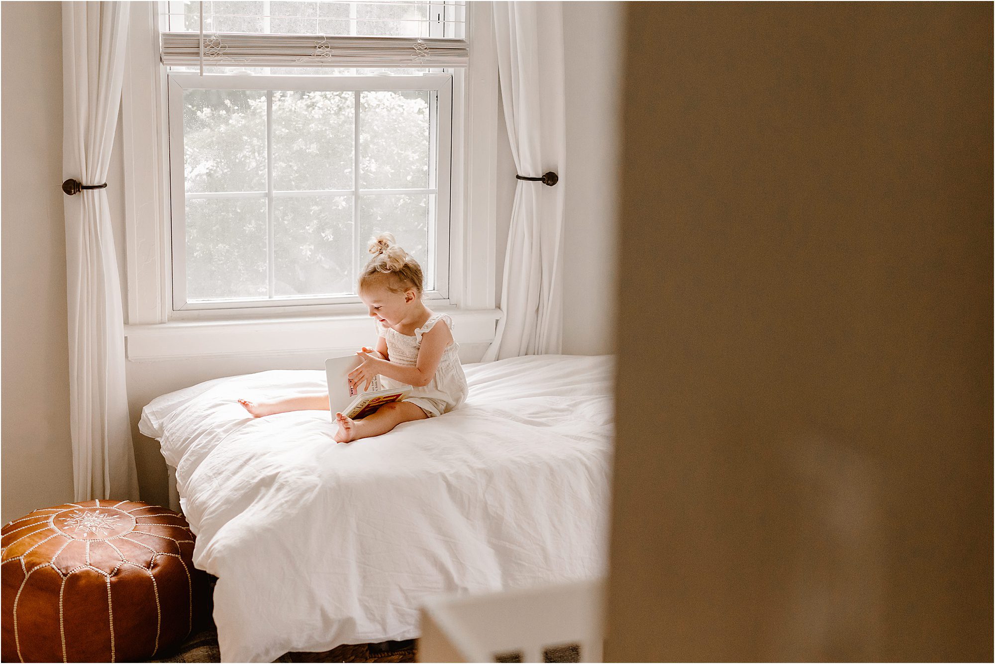 little girl sitting on her bed at home reading a book