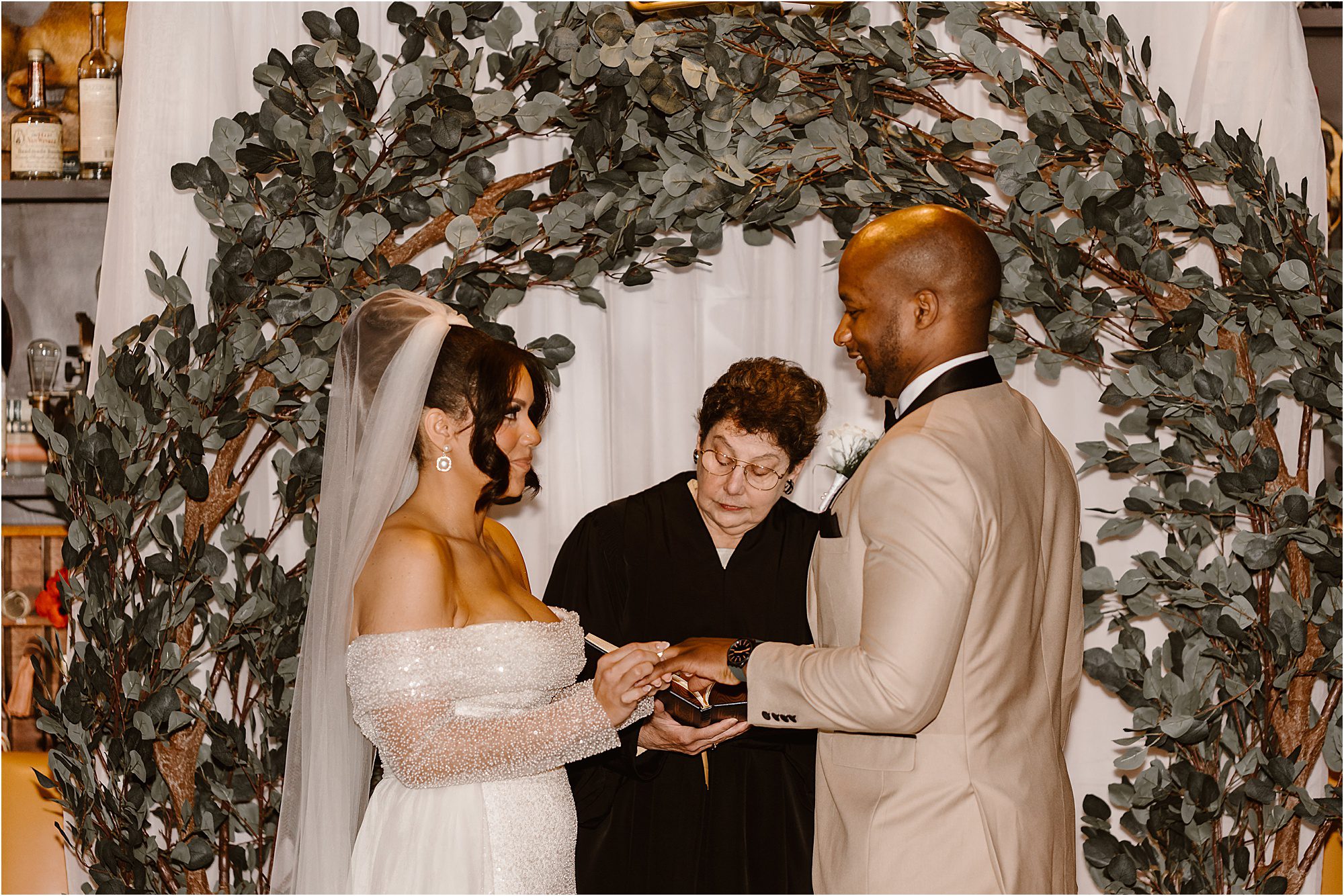 bride in white wedding dress and veil puts ring on groom