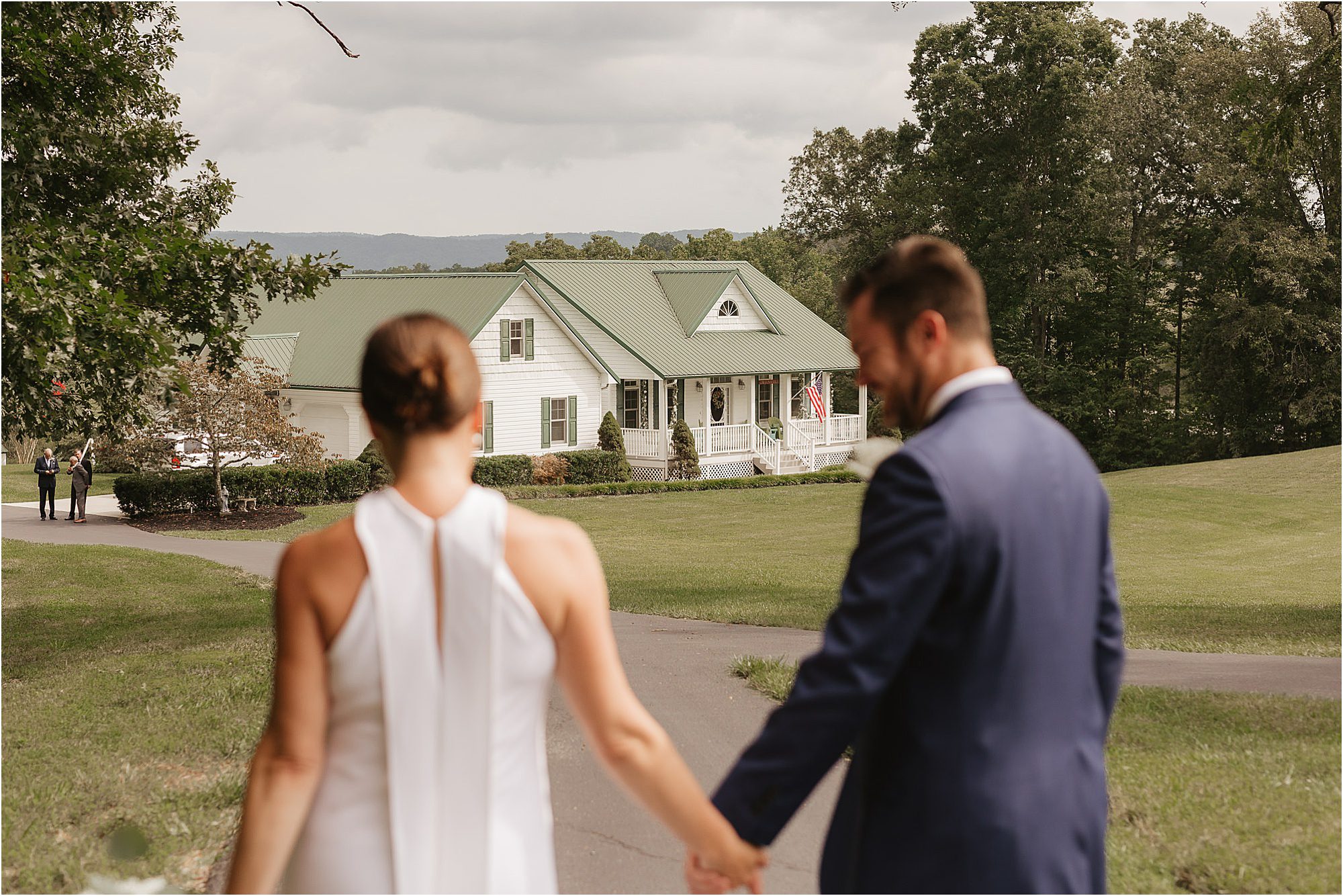 bride and groom hold hands while walking to white house with green roof