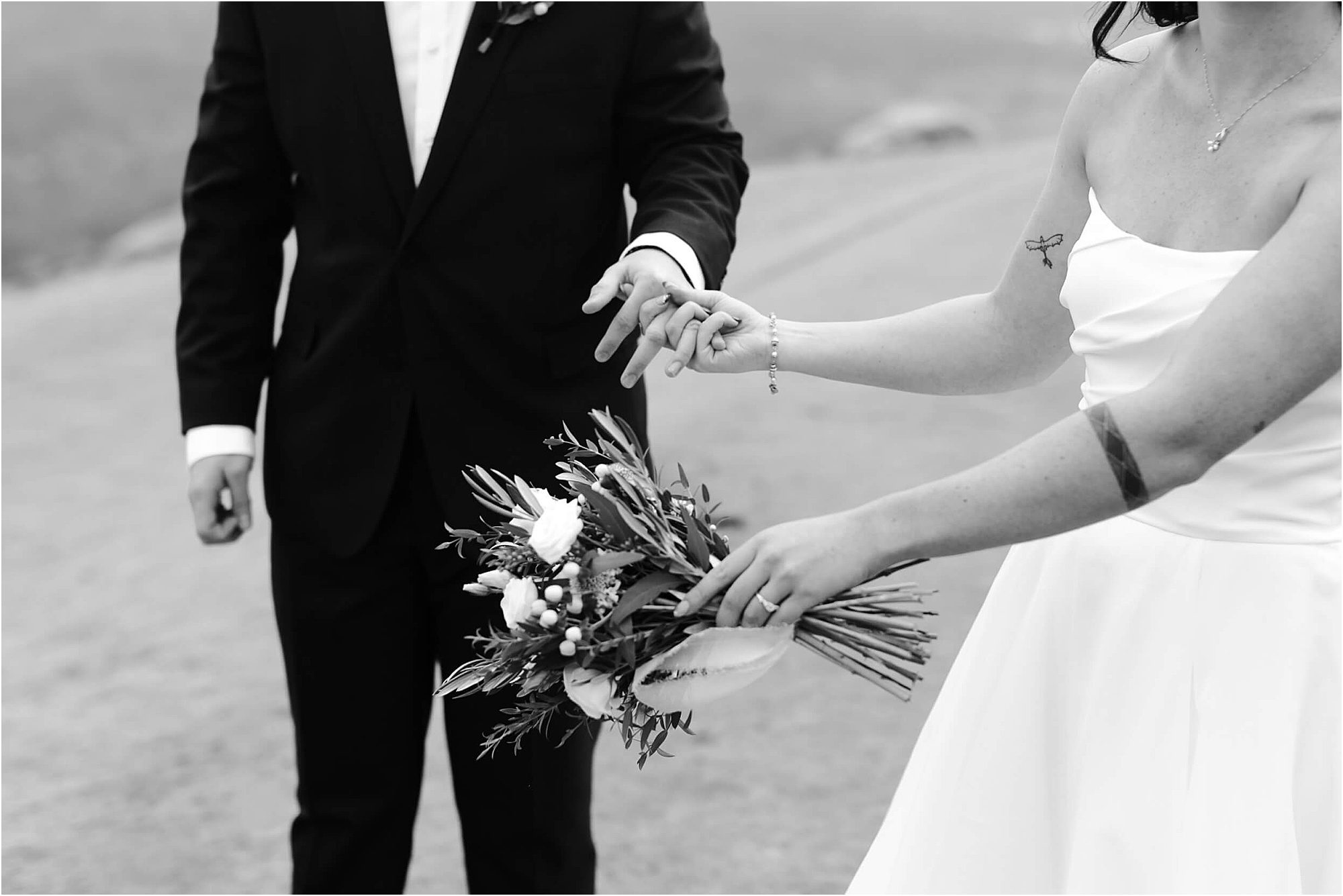 Black and white photo of a bride in a strapless dress holding a bouquet, gently touching the hand of a groom in a suit. Their faces are out of frame, capturing an intimate moment from a wedding at Cloudland at McLemore Resort.